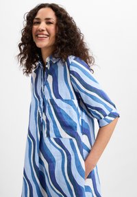 Blau-weiß gestreiftes Kleid mit hochrollbaren Ärmeln, das über eine Brusttasche und eine lockere Passform verfügt. Der Stoff hat eine leichte, strukturierte Optik.