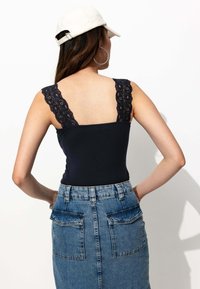 Bodysuit marine à bretelles en dentelle, associé à une jupe en denim taille haute avec deux poches arrière et une finition délavée.