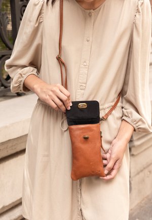 Brązowa skórzana torba na ramię z czarną tkaniną u góry, zamkiem błyskawicznym i ozdobnymi elementami. Gładka faktura, smukły kształt, idealna na najważniejsze rzeczy.