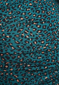 Tissu bleu sarcelle avec un imprimé léopard noir et beige et des lignes de couture horizontales visibles créant de légers fronces.