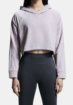 Haut à capuche court de couleur rose clair avec capuche, manches raglan et détails sur les coutures latérales, associé à des leggings gris foncé avec un imprimé de logo discret.
