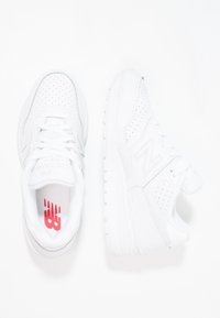 Bílé sportovní boty vyrobené z kůže a síťoviny, s perforovanými detaily, šněrováním, polstrovaným vnitřkem a červeným logem na stélce.