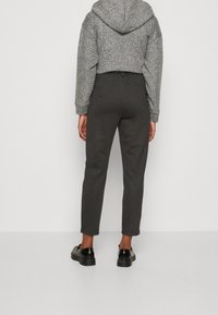 Kort hoodie i grått texturerat tyg med huva. Matchad med mörkgrå avsmalnande byxor. Svarta skor med kraftiga sulor.