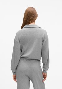 Grau Sweatshirt mit lockerer Passform, überschnittenen Schultern und einem Kragen. Der Stoff wirkt weich und strukturiert, kombiniert mit passenden grauen Hosen.