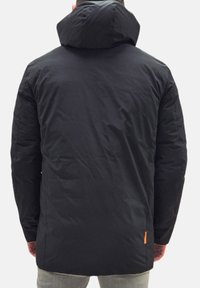 Giacca imbottita nera con cappuccio, caratterizzata da una texture liscia e un accento arancione sul lato, vista da dietro.