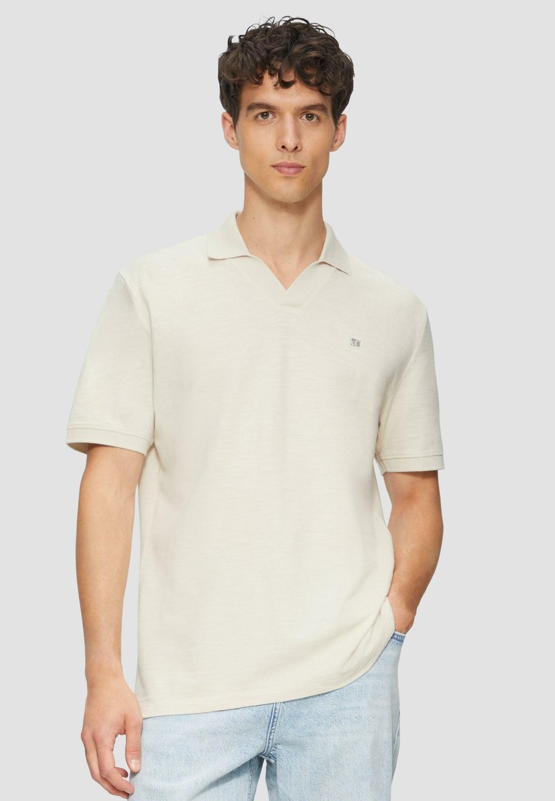 Beige polo shirt met korte mouwen en een V-hals, voorzien van een klein logo aan de linkerkant. Gemaakt van zachte, gestructureerde stof.