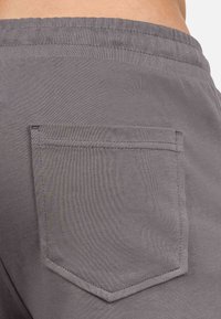 Shorts in cotone grigio con una tasca posteriore di forma rettangolare e bordi cuciti, che mostrano un tessuto liscio e texture.