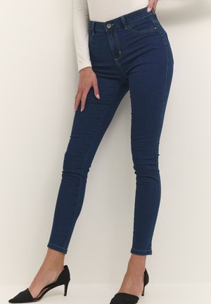 Dark blue skinny jeans made of denim; high-waisted with five-pocket design, button closure, and slight fading on thighs. Black high-heeled shoes.