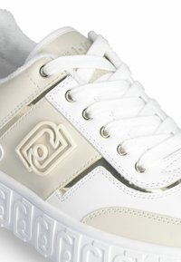 Sneakers bianchi e crema chiara con una tomaia sintetica liscia, punta rotonda, accenti metallici e una suola bianca texturizzata.
