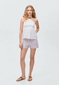 Top bianco a fascia con vita arricciata, abbinato a pantaloni corti viola chiaro e infradito marroni. Tessuto strutturato e vestibilità rilassata.