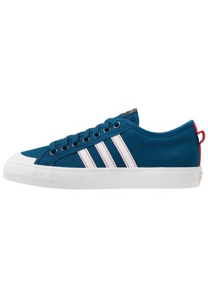 Niskie niebieskie sportowe buty z białą gumową podeszwą, białym wzorem z trzema paskami, ciemnoniebieskimi sznurowadłami i czerwoną pętlą na pięcie.