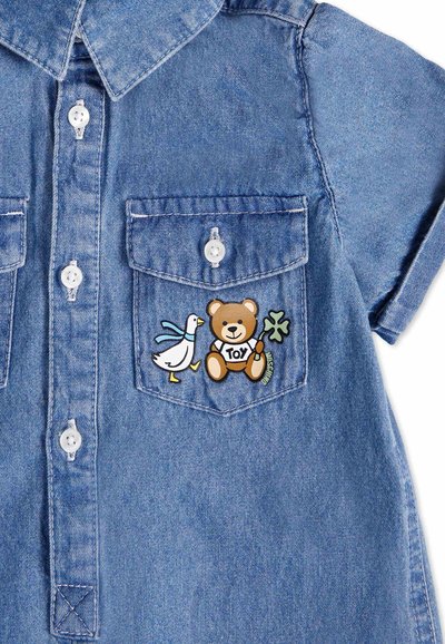 Camicia in denim di colore blu, con colletto e tasche anteriori. La tasca sinistra presenta una patch colorata con un orso e un'anatra.