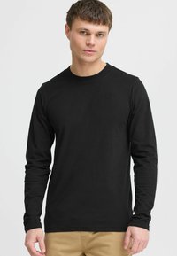 Black long-sleeve t-shirt made of soft cotton fabric. Features a round neckline and a small, tonal logo accent on the chest.