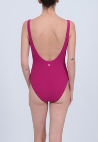 Maillot de bain une pièce fuchsia avec un dos décolleté et des bretelles fines, fabriqué à partir d'un tissu lisse. Présente un petit logo à l'arrière.