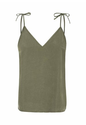 Blondynka w ciemnym topie i czarnych szortach opiera się o biały pojazd przy skalistej plaży z spokojną wodą i czystym niebem.