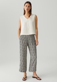 Witte mouwloze top met een gestructureerde brei, gecombineerd met loszittende zwart-wit gestreepte broek met een bladdesign. Zwarte schoeisel.