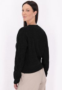 Pulover negru din tricot cu model, cu decolteu rotund, mâneci lungi și o textură interesantă. Purtați cu pantaloni deschisi la culoare.