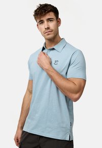 Svijetloplava polo majica izrađena od mekanog materijala, s klasičnom kragnom, kratkim rukavima i malim izvezenim logotipom na prsima.