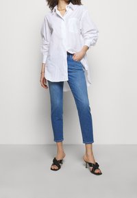 Vit skjorta med knäppning fram och en enda bröstficka, matchad med ljusblå jeans och svarta klacksandaler med knutdetalj.