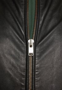 Černá kožená bunda s centrálním zlatým zipem. Taháček zipu má vyryté "SELECTED", s hladkým povrchem a dobře padnoucím střihem.