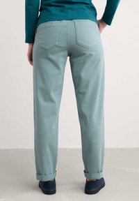 Pantaloni azzurri chiari, dalla vestibilità ampia e cintura arrotolata, con tasche posteriori e una texture liscia. Abbinati a scarpe blu navy.