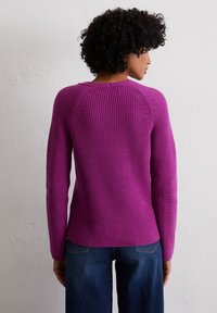 Lila gerippter Strickpullover mit langen Ärmeln, ausgestattet mit einem geschwungenen Saum und zarten Spitzenakzenten an den Ärmeln.
