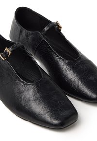 Zapatos de piel sintética negra con punta afilada y correa en el tobillo. Superficie texturizada con un acabado brillante y un pequeño detalle de hebilla dorada.