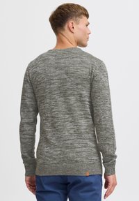 Maglione grigio lavorato a maglia con un motivo mélange strutturato. Collo a giro, maniche lunghe e polsini a coste. Presenta una piccola etichetta in pelle del marchio all'orlo.