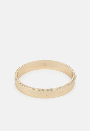 Bracelet jonc en métal doré avec bords perlés et texte en cursive gravé sur le côté extérieur, présenté sur un fond blanc.