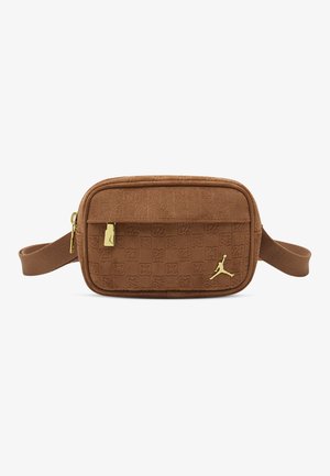 Sac banane en tissu marron avec un motif de logo en relief, une fermeture éclair dorée et un accent logo Jumpman doré sur le devant. Forme rectangulaire compacte.