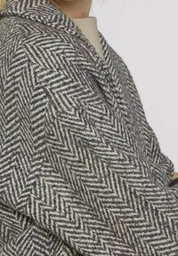Cappotto in lana a motivo spina di pesce grigio e crema, caratterizzato da una finitura testurizzata e un colletto a scialle, con cuciture visibili e vestibilità rilassata.