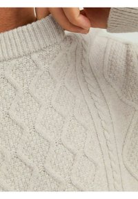 Light gray knitted sweater with textured diamond and cable patterns. Features a ribbed crew neckline. Soft, thick yarn texture.