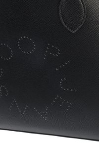 Bolsa de couro preta com padrões em relevo de pontos formando letras, textura suave, forma estruturada e detalhes de costura subtis.