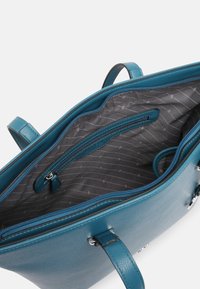 Sac à main en cuir turquoise avec un intérieur ouvert, présentant un motif doublé gris, une poche zippée et deux poignées pour le transport.