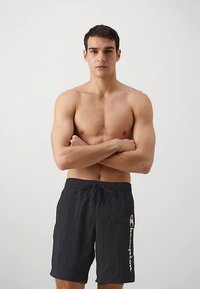 Șort de baie negru cu talie elastică și șnur, având un logo alb pe lateral. Material ușor, cu textură netedă.