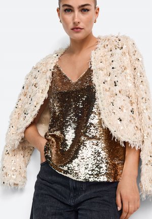 Beige fuskpälsjacka med glittrande, paljetterad bronstopp. Texturerad, lös passform med V-ringning och svarta denimbyxor.