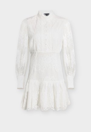 Robe courte blanche en dentelle à manches longues avec col montant, boutons recouverts de tissu sur le devant, taille cintrée et ourlet volanté évasé.