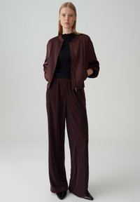 Burgundy bomber jacket with ribbed collar, paired with matching wide-leg pants. Both are made of smooth fabric. Black fitted top underneath.