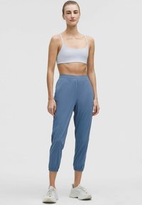Pantalones cortos de color azul claro con puños elásticos, combinados con un sujetador deportivo gris. Textura suave, diseñados para uso atlético, con un corte ajustado.