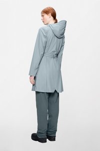 Ανοιχτό γκρι αδιάβροχο παλτό με κουκούλα, ζώνη στη μέση και μακριά μανίκια. Συνδυάζεται με σκούρο γκρι αδιάβροχο παντελόνι και μαύρα παπούτσια.