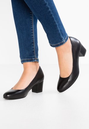 Zwarte leren hakken met een ronde neus en een chunky hak. Draag met blauwe jeans, wat de gladde textuur en het klassieke ontwerp benadrukt.