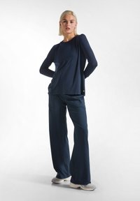 Maglia blu navy a maniche lunghe con un fit rilassato e scollo rotondo, abbinata a pantaloni larghi blu navy e scarpe da ginnastica chiare.