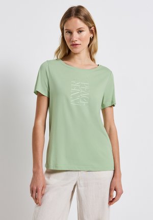 T-shirt à manches courtes de couleur vert clair en coton doux. Présente une impression sur le devant avec les mots "PAIX INTÉRIEURE" en alignement vertical. Encolure arrondie.