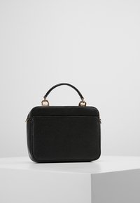 Sac à main en cuir noir avec une forme structurée, une anse supérieure et une surface texturée. Présente des accessoires dorés et une fermeture éclair.