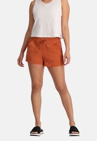 Oranje shorts met een trekkoord in de taille, voorzakken en een gladde textuur. Gecombineerd met een witte mouwloze top en zwarte slidesandalen.