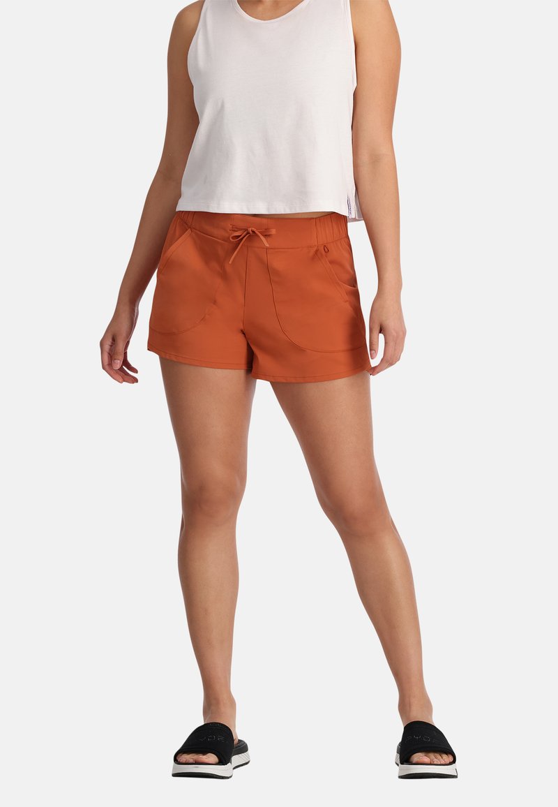 Oranje shorts met een trekkoord in de taille, voorzakken en een gladde textuur. Gecombineerd met een witte mouwloze top en zwarte slidesandalen.
