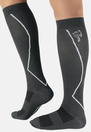 Schwarze kniehohe Socken mit geripptem Muster, weißen Akzentlinien und Logo, verstärktem Fußbett und gepolstertem Knöchelschutz.