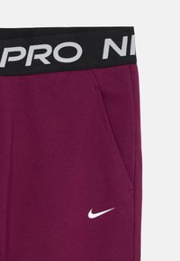Tumši violeta sporta bikses ar melnu elastīgu jostu, kurā baltā krāsā ir rakstīts "NIKE PRO". Mazs balts Nike logo netālu no kabatas. Mīksts materiāls.