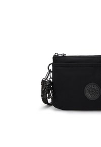 Sort nylon pouch med lynlås, en tekstureret logo-plade og en dekorativ sort charm. Kompakt rektangulær form.
