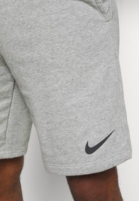 Grå bomullsshorts med en slät textur, med en svart Nike-logga på vänster sida nedtill och sidofickor.